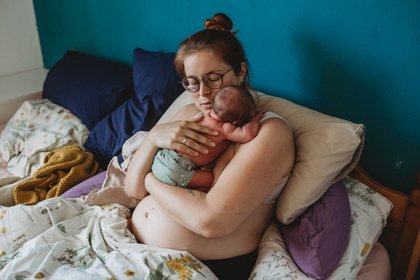 Mama kuschelt mit neugeborenem Baby im Bett beim Newobornshooting in München